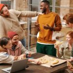 A group of diverse friends laughing and enjoying pizza together indoors.